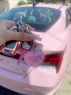 a person holding keys to a pink car with a hello kitty keychain on it