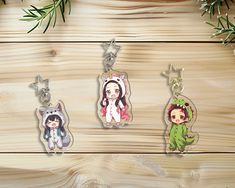 three keychains with cartoon characters on them sitting on a wooden table next to pine branches