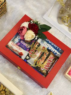 a red box filled with candy and flowers on top of a white fur covered floor