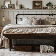 a bed with white sheets and pillows in a bedroom next to a wooden shelf filled with pictures