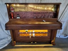 an old wooden piano with wine glasses on it's shelf and lights in the back