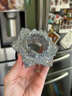 a person holding up a glass object in front of a refrigerator freezer with magnets on it