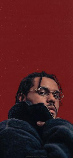 a man wearing glasses and a black jacket with his hands on his chest, standing in front of a red wall