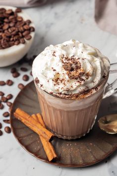 hot chocolate with whipped cream and cinnamon sticks on a plate next to some coffee beans