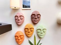 five different colored clay faces on a white wall next to a pineapple and potted plant