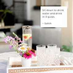 there is a tray with flowers and glasses on it, along with a sign that says sit down to drink water and drink in 3 cups