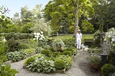 a woman standing in the middle of a garden filled with lots of trees and plants