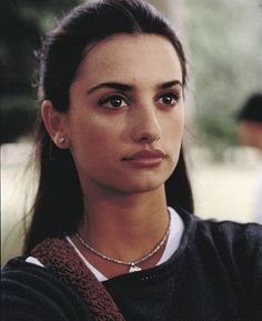 a close up of a person wearing a sweater and necklace with trees in the background