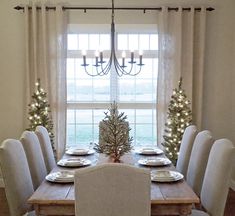 a dining room table set for christmas with white chairs and lights on the windowsill