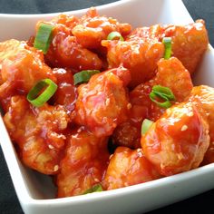 a white bowl filled with chicken covered in sauce and garnished with green onions