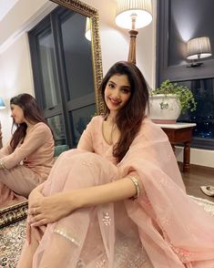 a woman sitting on the floor in front of a mirror wearing a pink dress and smiling