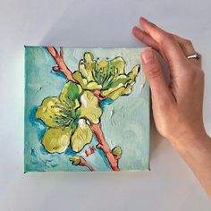 a hand is holding up a painting with yellow flowers on it