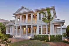 a large white house with lots of windows and palm trees in the front yard at dusk