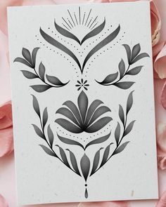 a white card with black and grey designs on it next to some pink flowers in the background