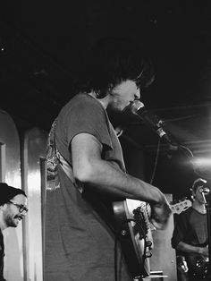 two men are playing guitars and singing into microphones while another man stands behind them