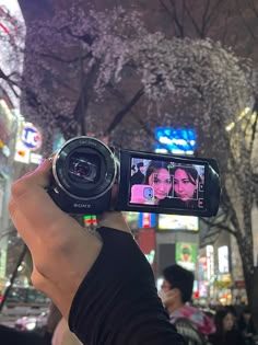 a person holding up a camera in front of a tree with pink blossoms on it