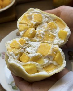 someone holding two halves of fruit on a plate with other food items in the background