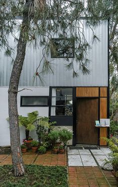 a house that is next to a tree and some plants in front of the door