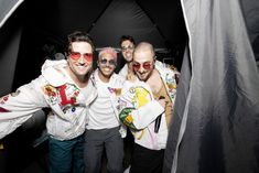 three men in white jackets and red sunglasses are posing for a photo inside a tent