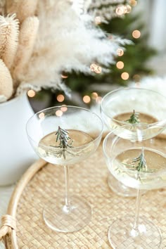 three wine glasses sitting on top of a wicker tray next to a christmas tree