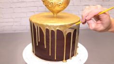 a person is decorating a chocolate cake with gold icing and a heart on top