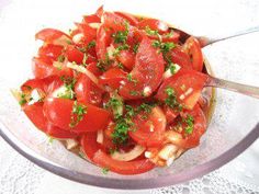 a glass bowl filled with sliced tomatoes and herbs