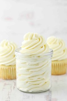 three cupcakes with white frosting in a glass jar