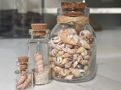 several sea shells in glass jars on a counter top next to corks and bottles