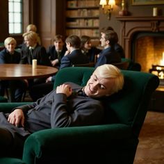 a woman laying on a green chair in front of a fire place with other people sitting around