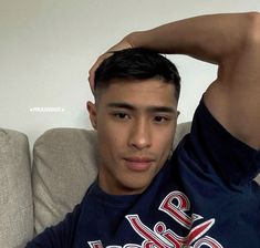 a young man sitting on top of a couch next to a white wall and looking at the camera