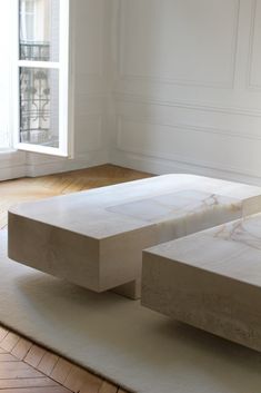 two white marble tables sitting on top of a rug in front of an open window