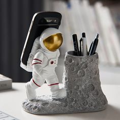 PRICES MAY VARY. Cute and Functional Pencil Holder and Phone Stand for Desk: An astronaut figurine with pencil holder and phone stand design, which combines creative appearance with practical use in mind. It perfectly holds scissors, pencils, makeup brushes, or small plants organized in style. Meanwhile, it is hold all mobile phones from 4-8 inches. Decorative Pen Holder with Phone Stand: The hand-painted sculpture with a pencil holder & phone holder makes a beautiful and appealing look. Perfect for displaying this simple yet eye-catching phone holder in your room for a funny addition to your home office. Sturdy and Durable: Measuring 6.7"W x 3.94"D x 6.3"H. The cool astronaut figurine is composed of sturdy resin material. It is well weighted to ensure that it stands up and holds your stat Phone Stand Design, Space Lovers Gifts, Pen Container, Phone Pen, Phone Stand For Desk, Pen Pencil Holder, Decorative Bookends, Pen Storage, Space Lovers