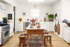 a kitchen with white walls and wooden floors has an island table surrounded by stools