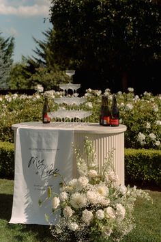 a table topped with bottles and vases filled with white flowers on top of a lush green field