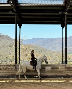 a woman riding on the back of a white horse next to a wooden bench under a roof