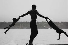 a man and two children are playing with each other on the beach by the water