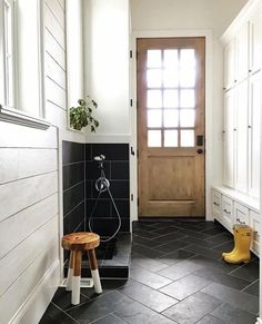 a bathroom with black and white tile flooring next to a wooden door, yellow rubber boots on the ground