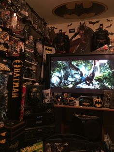 a batman movie is on the tv screen in this room with many other toys and collectibles