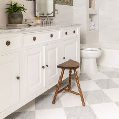 a white bathroom with checkered floor and wooden stool