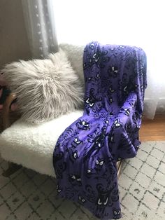 a purple blanket sitting on top of a white chair next to a gray and black pillow