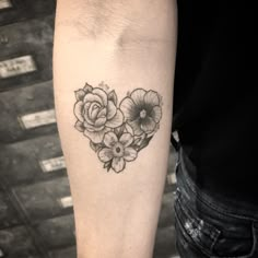 a black and white photo of a flower heart tattoo on the left arm, with three flowers in it