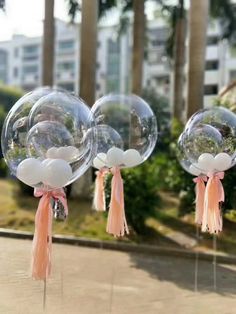 three clear bubble balloons with tassels and bows hanging from them on poles in front of trees