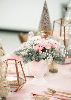 a table topped with pink and white flowers next to small christmas trees on top of a table