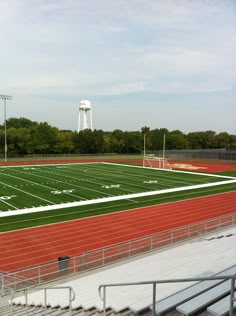 an empty football field in front of a white water tower with trees on the other side