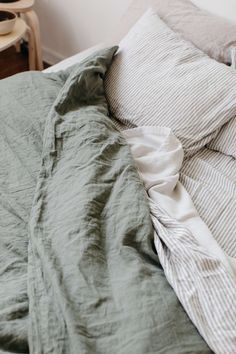 an unmade bed with two pillows on top of it and a green comforter