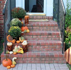 pumpkins and gourds are placed on the steps to a home's front door