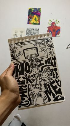 a person holding up a notebook with drawings on it