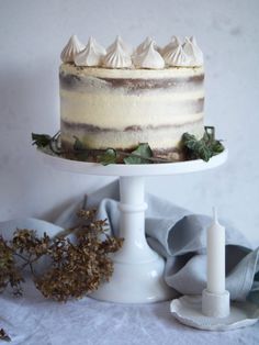 a cake with frosting and greenery on a white pedestal next to a candle