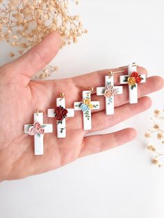 a person's hand holding seven crosses with flowers on them