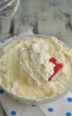 a bowl filled with white frosting on top of a blue polka dot table cloth